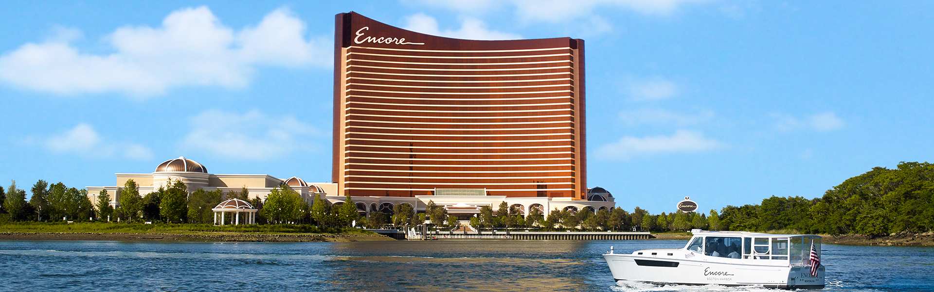 The exterior of Encore Boston Harbor with a boat driving by in the water