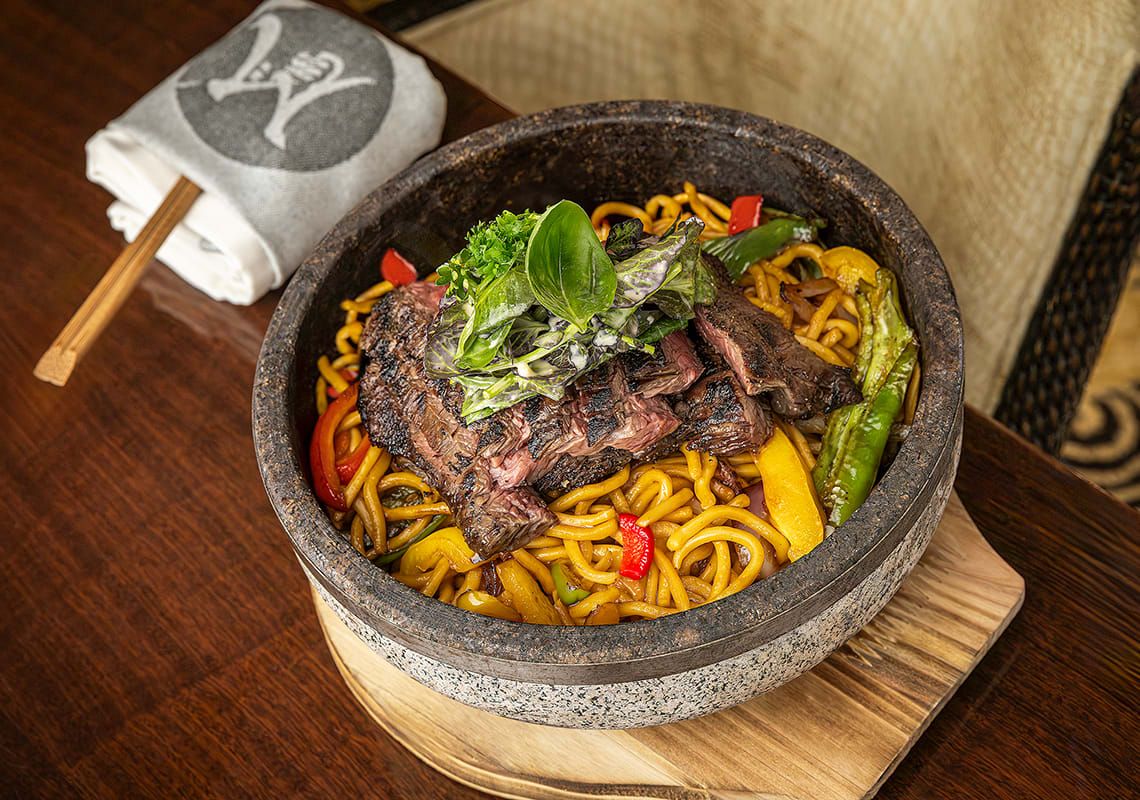 Slices of steak sit on top of a bowl of noodles
