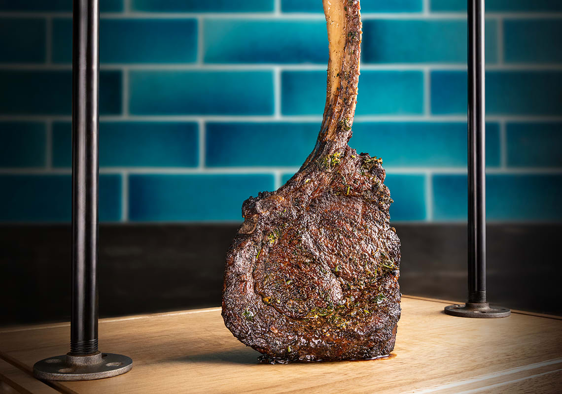 A bone-in tomahawk steak sits on a wood platter