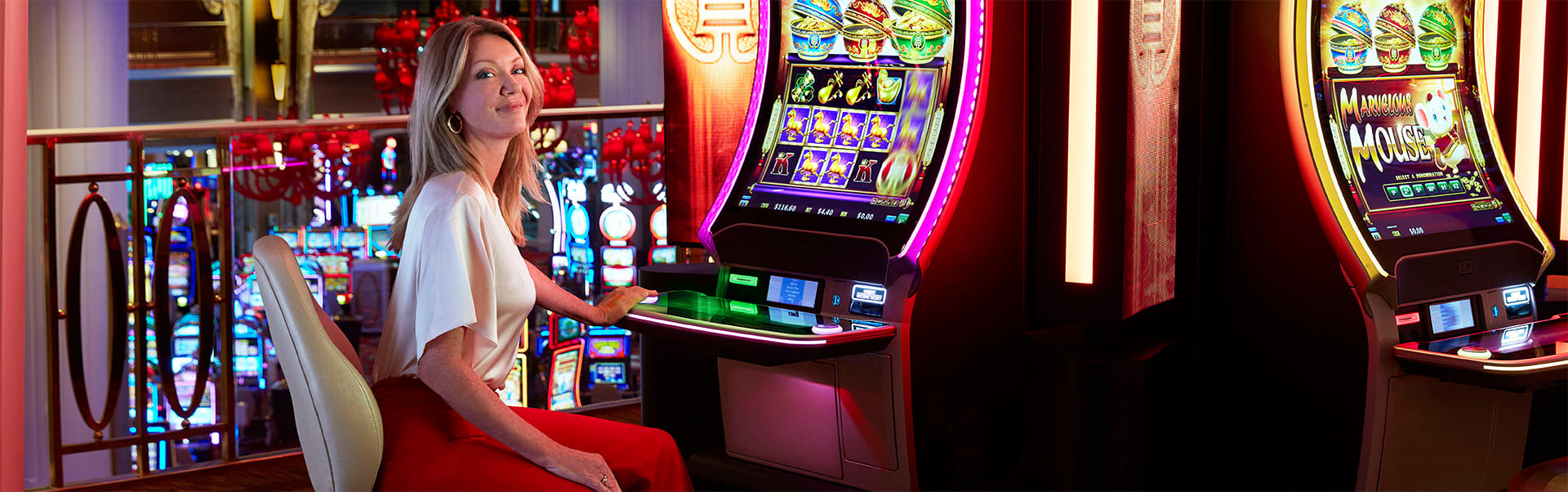 A woman in a white shirt and red pants sits at a slot machine