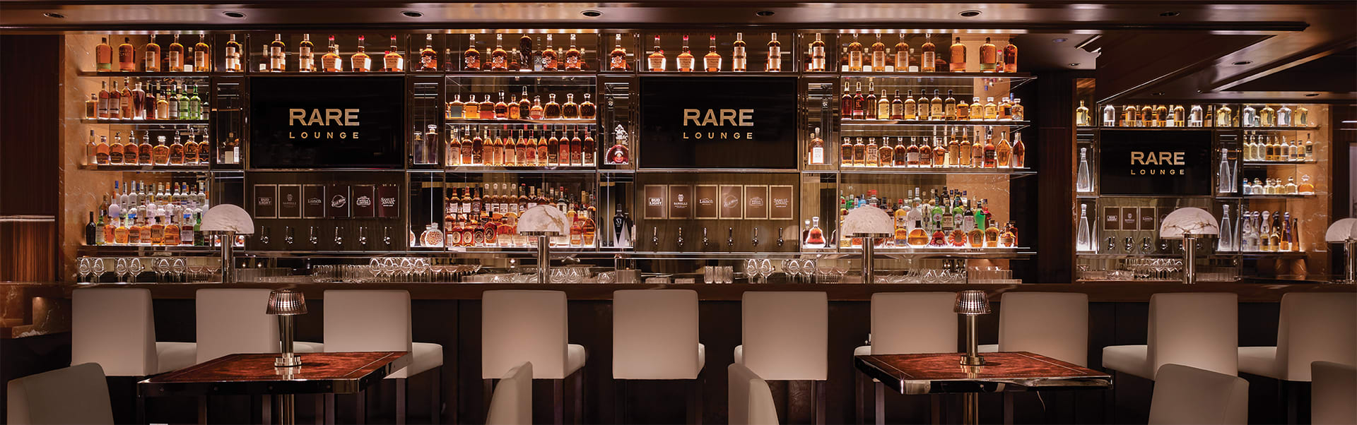 Several chairs and tables sit in front of a bar in the interior of Rare Lounge at Encore Boston Harbor